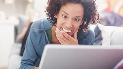 A woman smiling with a hand on her chin while looking at a laptop screen.
