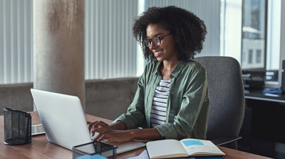 A woman sitting at her desk while smiling and typing on her laptop