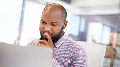 Man in business casual attire using a computer and holding hand on chin and one finger over his mouth.